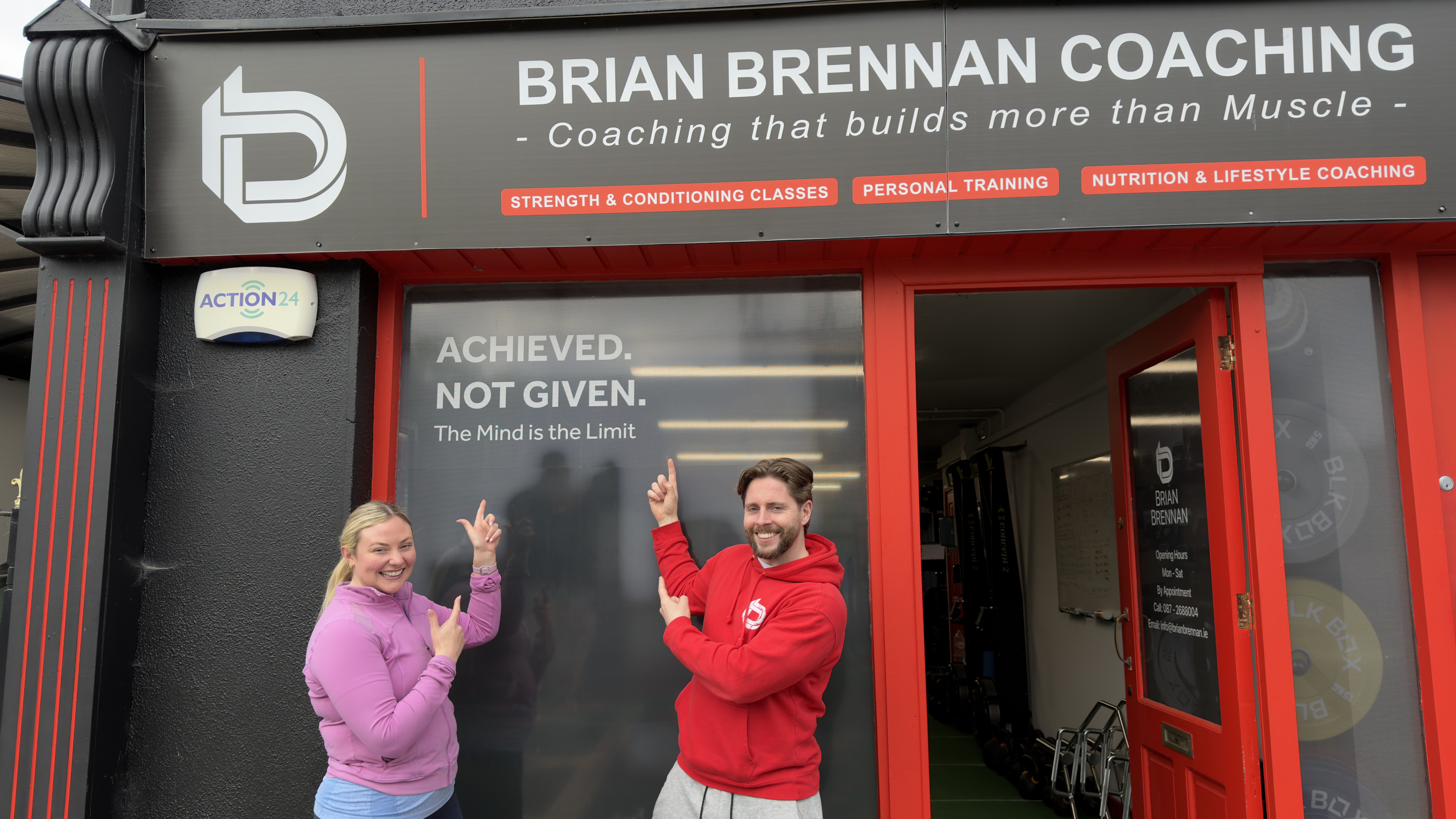 Brian Brennan, a fitness trainer, and his first client, Laura, point at a sign for his studio.