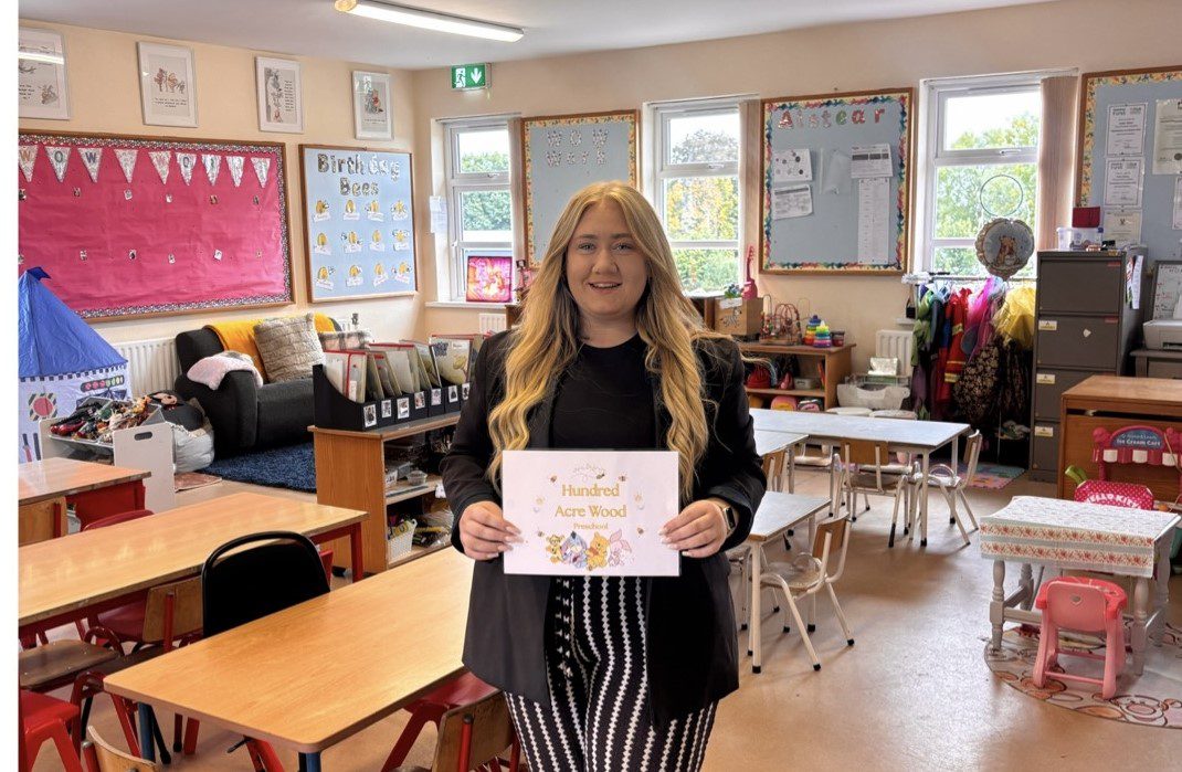Louise Killeen Caulfield, owner of Hundred Acre Wood Pre-school She's dressed in black and white striped trousers and a black top, and holds a sign reading, "Hundred Acre Wood Pre-school".