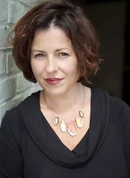 Acclaimed author with shoulder-length brown hair wearing a black shirt and a statement necklace with metallic geometric shapes at Salmon’s for her new book launch.